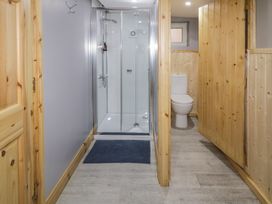 A bathroom with a glass shower enclosure wooden panel walls a toilet and a blue mat on the floor at Drumrane Lodge in Dungiven Londonderry