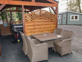 A wooden gazebo with a wicker table and chairs set and a hot tub under the shelter at Drumrane Lodge in Dungiven Londonderry
