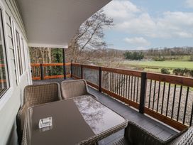 A balcony with wicker chairs and a table overlooking fields and trees at Railway Lodge in Dungiven Londonderry