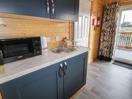 A kitchen area with a microwave, kettle, sink, wooden wall paneling, a door, curtain, and glass door leading outside at Railway Lodge in Dungiven Londonderry