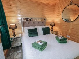A bedroom with a bed with green pillows and towels two bedside tables with lamps a round mirror on wooden walls at Railway Lodge in Dungiven Londonderry