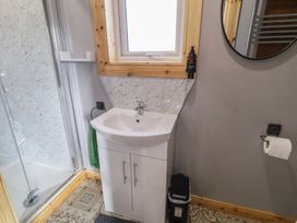 A bathroom with a white sink cabinet under a window a round mirror a shower stall and a toilet paper holder at Railway Lodge in Dungiven Londonderry