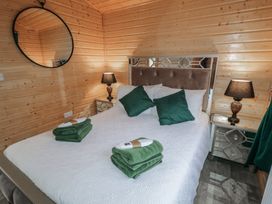 A bedroom with a bed with green pillows two nightstands with lamps and wooden walls at Railway Lodge in Dungiven Londonderry