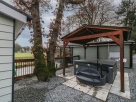 An outdoor area with a hot tub under a wooden canopy next to trees and a fenced grassy field at Railway Lodge in Dungiven Londonderry
