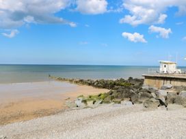 A beach with sand, rocks, sea, and a building at Highland House in Sheringham