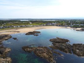 A coastal area with a sandy beach, rocky formations in the water, and houses along the shoreline at Seaddler in Trearddur Bay