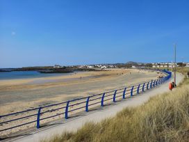 A sandy beach with a blue railing and pathway by the sea with houses in the distance at Seaddler in Trearddur Bay