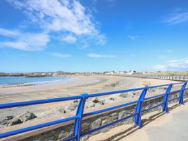 A beach with sand and rocks beside a walkway with blue railings at Seaddler in Trearddur Bay