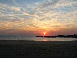 A beach with a calm sea and a sailboat during sunset at Seaddler in Trearddur Bay