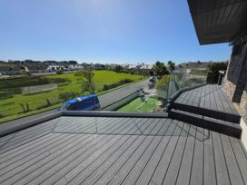 An outdoor deck with a glass railing overlooking a road and grassy area at Seaddler in Trearddur Bay