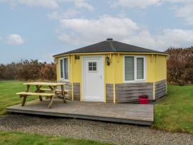 A small yellow and wooden cabin with a white door and windows a picnic table on a wooden deck and a pink flower pot near it at Hartland Quay near Hartland