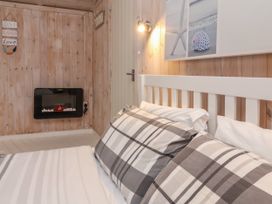 A bedroom with a bed with plaid pillows a wall-mounted electric fireplace wooden walls and a door at Hartland Quay near Hartland