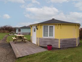 Two round cabins with wooden paneling and picnic tables outside on grassy area at Hartland Quay near Hartland