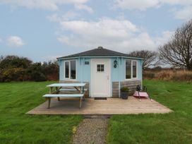 A small blue and wood hexagonal building with white door and windows with picnic table and wheelbarrow on wooden deck at Shipload Bay near Hartland