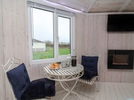 A small dining area with two cushioned chairs and a round table with cups and croissants near a window and a wall-mounted TV at Shipload Bay near Hartland