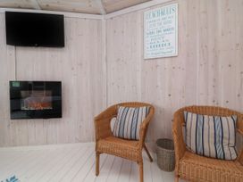 A room with two wicker chairs with striped cushions a wall-mounted electric fireplace a wall-mounted tv and a beach rules sign at Shipload Bay near Hartland