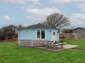 A small octagonal light blue cabin with a picnic table on a wooden deck in a grassy area at Shipload Bay near Hartland