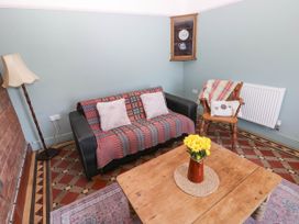 A living room with a sofa covered by a patterned throw pillows a wooden chair with a cushion and blanket wooden coffee table with flowers floor lamp and corner cabinet at Llanwern Farm Fishguard