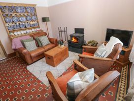 A living room with leather sofas, a wood-burning stove, a wooden chest coffee table, and a display of blue and white plates at Llanwern Farm in Fishguard