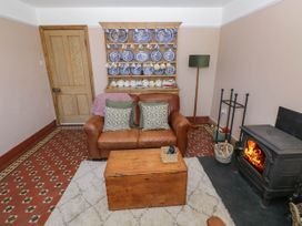 A living room with a brown leather sofa, wooden chest coffee table, blue patterned plates on a wooden rack, and a wood burning stove at Llanwern Farm in Fishguard