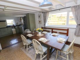 A dining area with a wooden table set for six and a kitchen with green cabinets in the background at Llanwern Farm in Fishguard