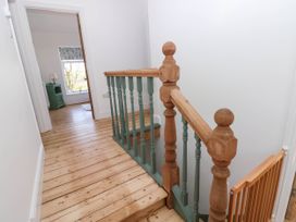 A hallway with wooden floor and staircase railing leading to a room with a window at Llanwern Farm in Fishguard