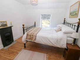 A bedroom with a metal frame bed a small fireplace a wooden nightstand and a rug on a wooden floor at Llanwern Farm in Fishguard