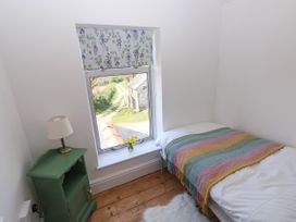 A small bedroom with a single bed with a striped blanket a green bedside table with a lamp and a window with floral blinds at Llanwern Farm in Fishguard