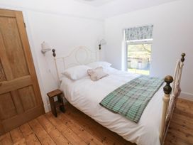 A bedroom with a white metal bed frame wooden floor and a window with floral blinds at Llanwern Farm in Fishguard