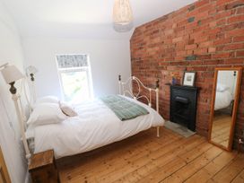 A bedroom with a bed, wooden floor, brick wall with a fireplace and a mirror at Llanwern Farm in Fishguard