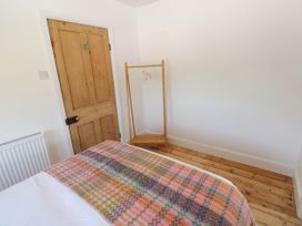 A bedroom with a wooden door a radiator a bed with a colorful blanket and a wooden clothes rack at Llanwern Farm in Fishguard