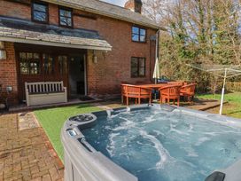 A backyard with a hot tub a wooden bench a dining table with chairs and an umbrella at Mill Cottage in Aylesbeare