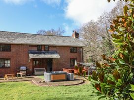 An outdoor patio area with a hot tub wooden bench table and chairs outside a brick house at Mill Cottage in Aylesbeare