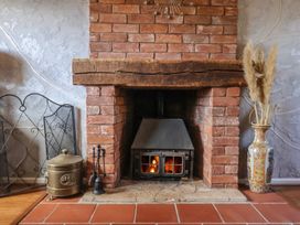 A brick fireplace with a wood stove insert burning firewood a metal fire screen a brass container fireplace tools and a vase with dried pampas grass Mill Cottage Aylesbeare