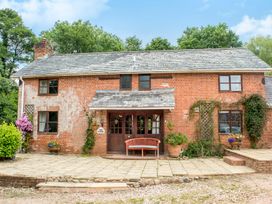 A brick house with a tiled roof and a wooden bench in front at Mill Cottage in Aylesbeare
