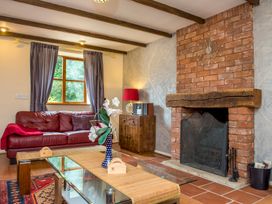 A living room with a red leather sofa a wooden cabinet a red lamp a glass coffee table a brick fireplace and window with curtains at Mill Cottage in Aylesbeare