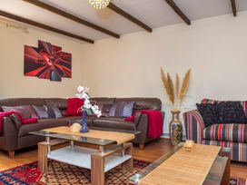 A living room with brown leather corner sofa and striped armchair with cushions a glass coffee table and a painting on the wall at Mill Cottage in Aylesbeare