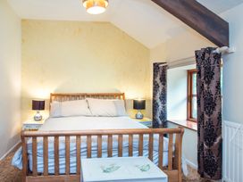 A bedroom with a wooden bed frame bedside tables with lamps patterned curtains and a window at Mill Cottage in Aylesbeare