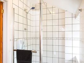 A tiled shower area with a glass door a black towel a showerhead and a soap dispenser at Mill Cottage in Aylesbeare