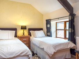 A bedroom with two single beds a nightstand with a lamp and a window with curtains at Mill Cottage in Aylesbeare