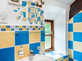 A bathroom with blue and yellow tiled walls a sink with a soap dispenser and glass holder a decorative mirror and a window at Mill Cottage in Aylesbeare