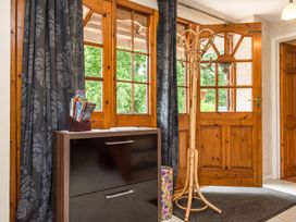An entryway with wooden double doors a coat rack a black cabinet with magazines and dark patterned curtains at Mill Cottage in Aylesbeare