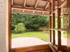 A wooden door open to a garden with a paved patio green grass a small tree and a wooden fence at Mill Cottage in Aylesbeare