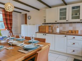 A kitchen with a wooden dining table set with plates and glasses next to white cabinets and a window with red curtains at Mill Cottage in Aylesbeare
