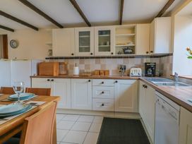 A kitchen with white cabinets wooden countertops a dining table with plates and glasses and kitchen appliances at Mill Cottage in Aylesbeare