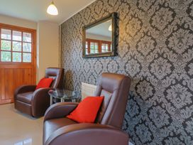 A seating area with two brown leather chairs and red cushions a glass side table a wall mirror and a wooden door at Mill Cottage in Aylesbeare