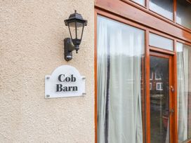 A wall with a light fixture and a sign that says Cob Barn next to a wooden framed glass door with curtains at Cob Barn in Aylesbeare