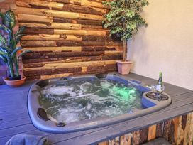 A hot tub with bubbling water beside two potted plants and a bottle of wine with two glasses at Cob Barn in Aylesbeare