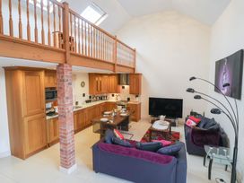 An open plan living room and kitchen with wooden cabinets a dining table two sofas and a television at Cob Barn in Aylesbeare