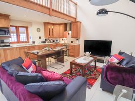 An open plan living area with blue sofas pink cushions a wooden dining table kitchen cabinets and a television at Cob Barn in Aylesbeare